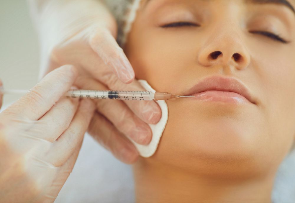 A person on Long Island, eyes closed, receives a cosmetic procedure as a gloved hand expertly administers a lip injection with a syringe.