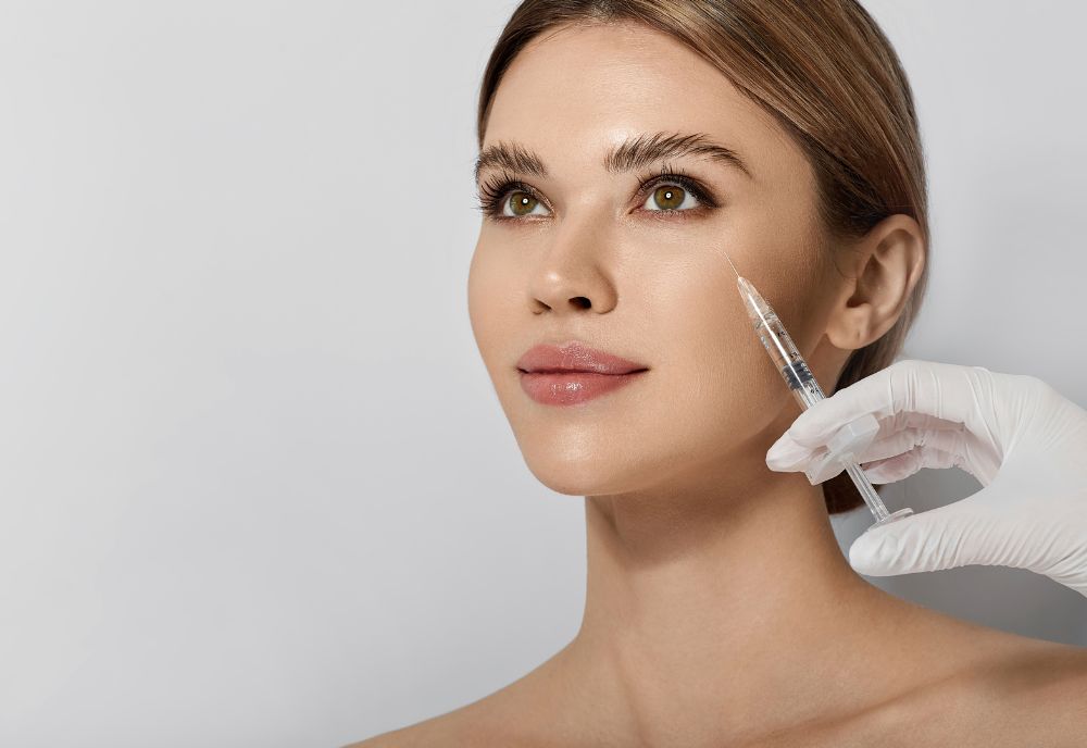 A person on Long Island receives a cosmetic injection in the cheek by a gloved hand, showcasing advanced treatments against a neutral background.