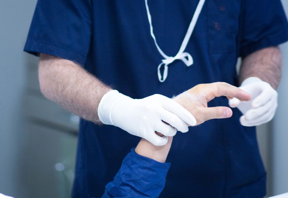 A healthcare professional wearing gloves examines a patient's hand in a clinical setting.