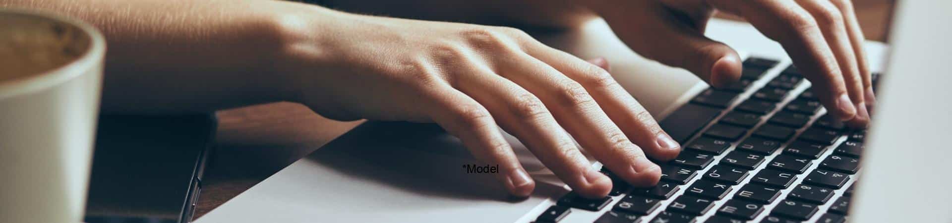 Hands typing on a laptop keyboard, with a coffee cup nearby on a wood surface. On Long Island, people often juggle tech tasks while seeking effective carpal tunnel treatment solutions to maintain their productivity and comfort.