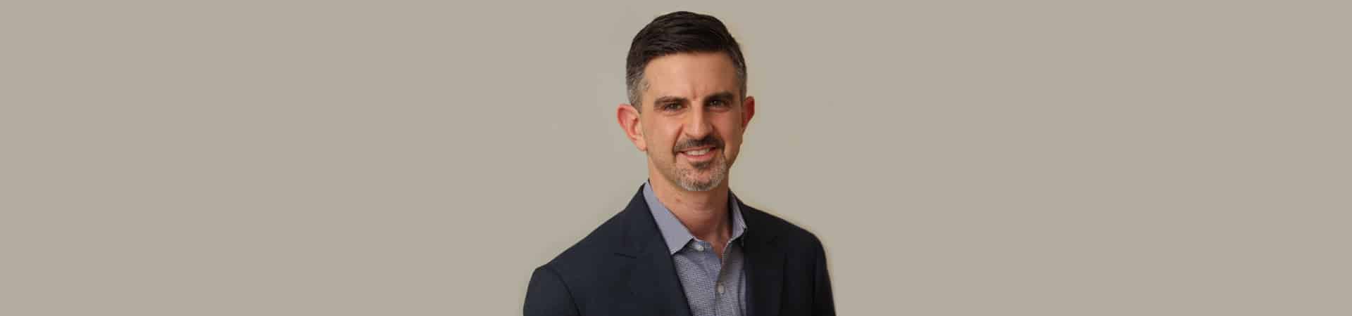 Brian A. Pinsky, MD, FACS, with short dark hair and a beard, smiles warmly while donning a dark suit jacket over a collared shirt, set against a plain background.