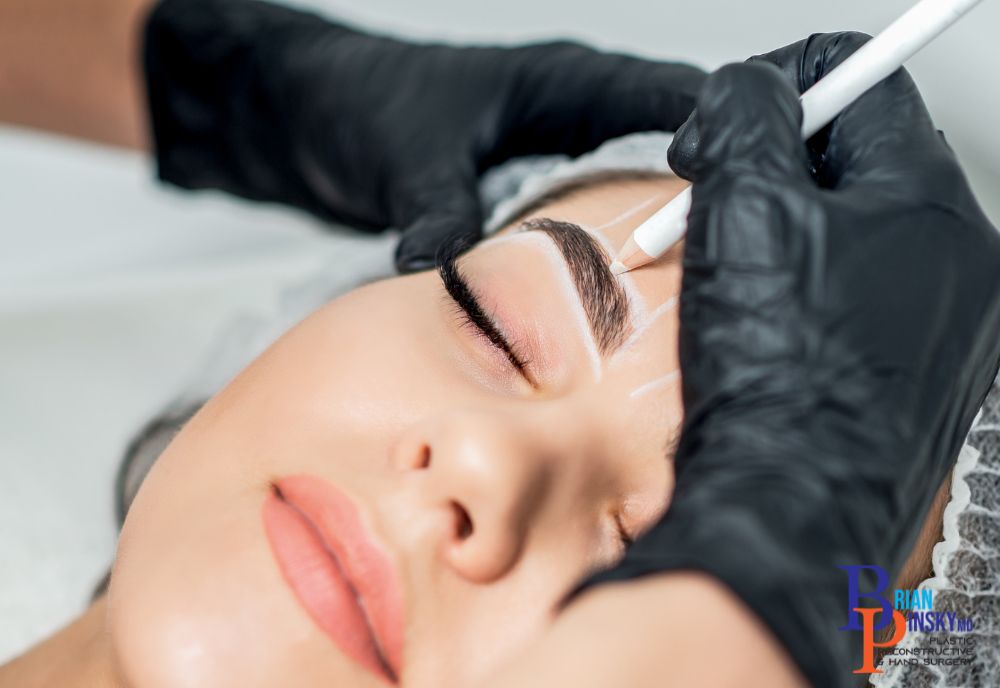 A serene person with closed eyes receives a precise eyebrow shaping using a white pencil by gloved hands—an artful cosmetic procedure enhancing natural beauty.