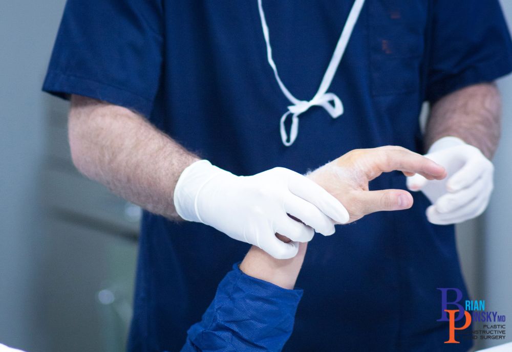 A person in blue scrubs and gloves examines a patient's hand, meticulously evaluating it as part of a treatment procedure in a Long Island medical facility.