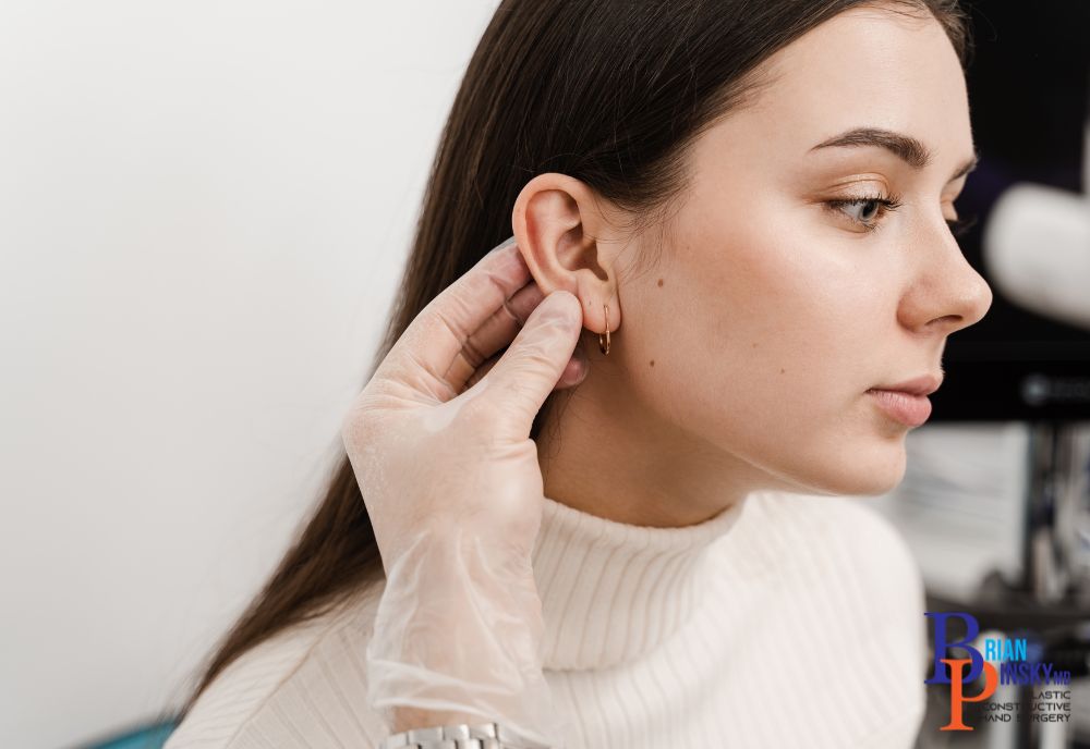 A person in a white sweater is having their ear examined by a gloved professional, possibly considering cosmetic procedures.