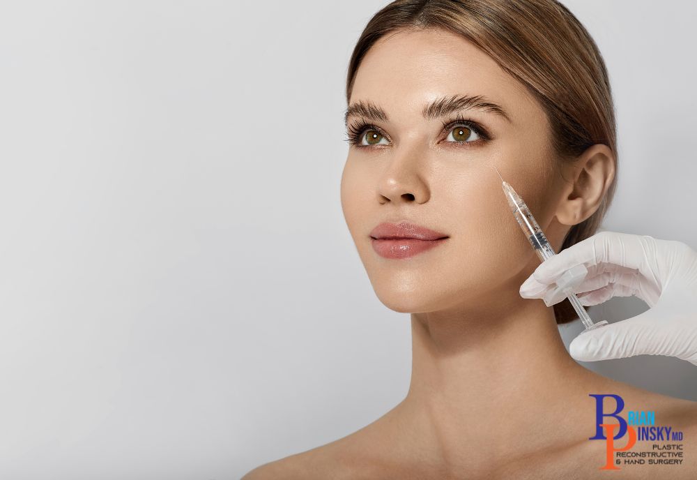 A woman with bare shoulders looks up as a gloved hand approaches her face with a syringe, preparing for the cosmetic procedure.