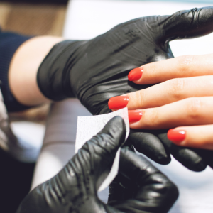 A hand specialist on Long Island wearing black gloves carefully cleans another person's nails, which are painted red.