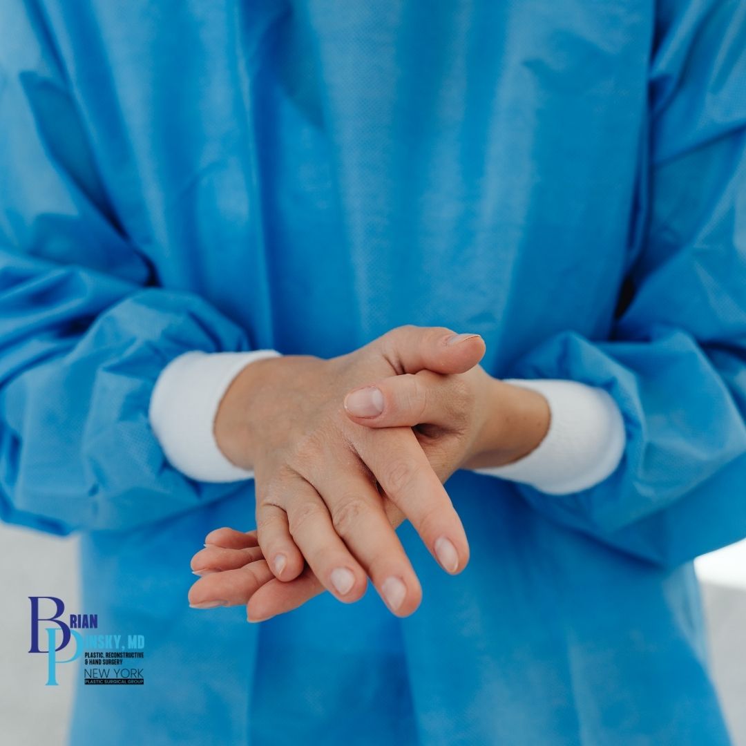 Person in blue medical scrubs rubs their hands together, shown from the neck down. A medical practice logo is visible in the corner, highlighting expertise in hand surgery in Babylon.