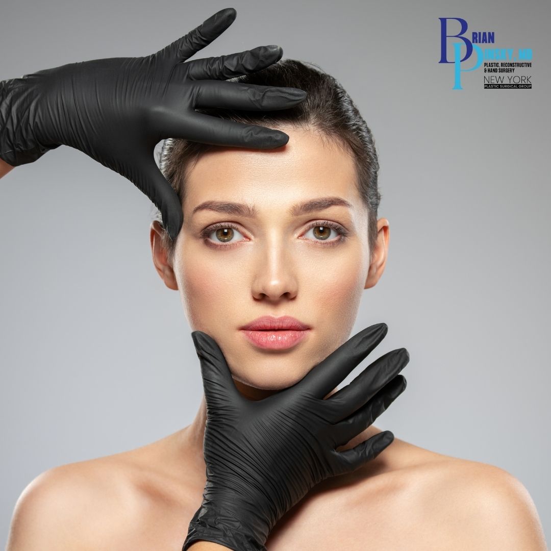 A woman's face is framed by two gloved hands, highlighting expert plastic surgery in Huntington NY, with a clinic logo displayed in the top right corner.