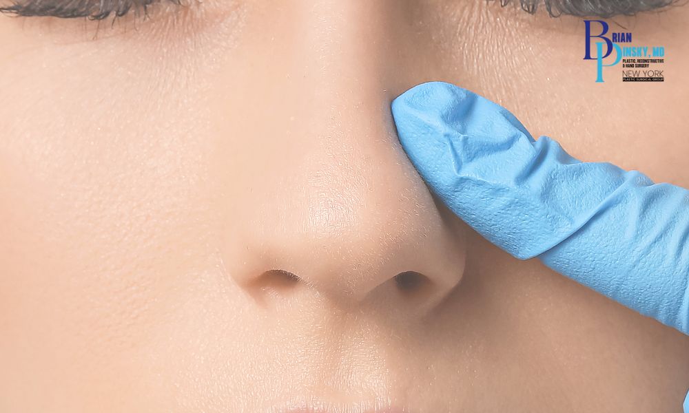 A gloved hand touches the side of a person's nose, suggesting a rhinoplasty consultation, with a logo and text in the upper right corner. Perfect for practices based on Long Island. A gloved hand touches the side of a person's nose, suggesting a rhinoplasty consultation, with a logo and text in the upper right corner Perfect for practices based on Long Island