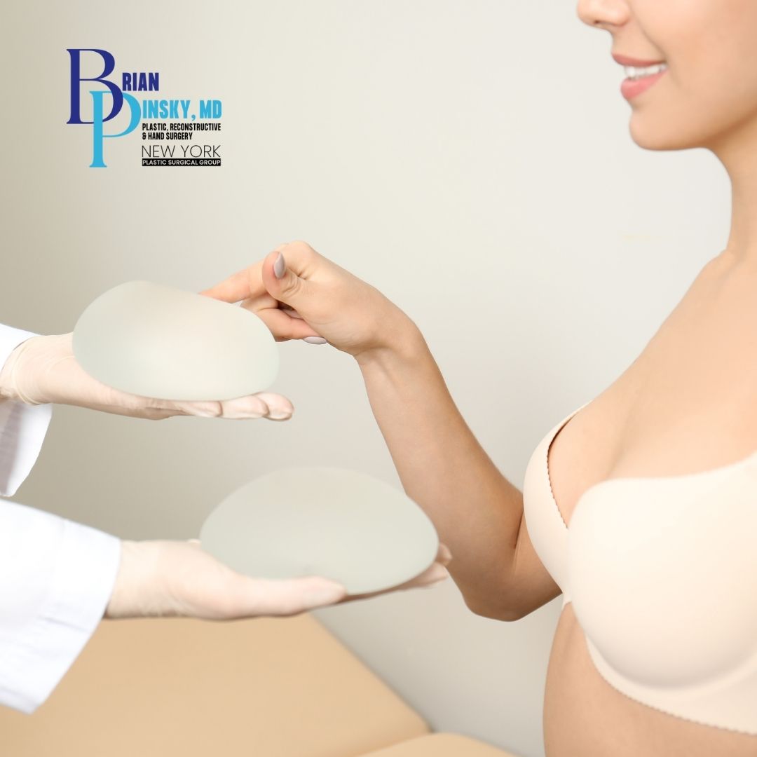 A woman in a beige bra selects a breast implant for breast augmentation from two options presented by a gloved medical professional. Dr. Brian Pinsky's clinic logo appears in the top left corner. A woman in a beige bra selects a breast implant for breast augmentation from two options presented by a gloved medical professional Dr Brian Pinsky's clinic logo appears in the top left corner